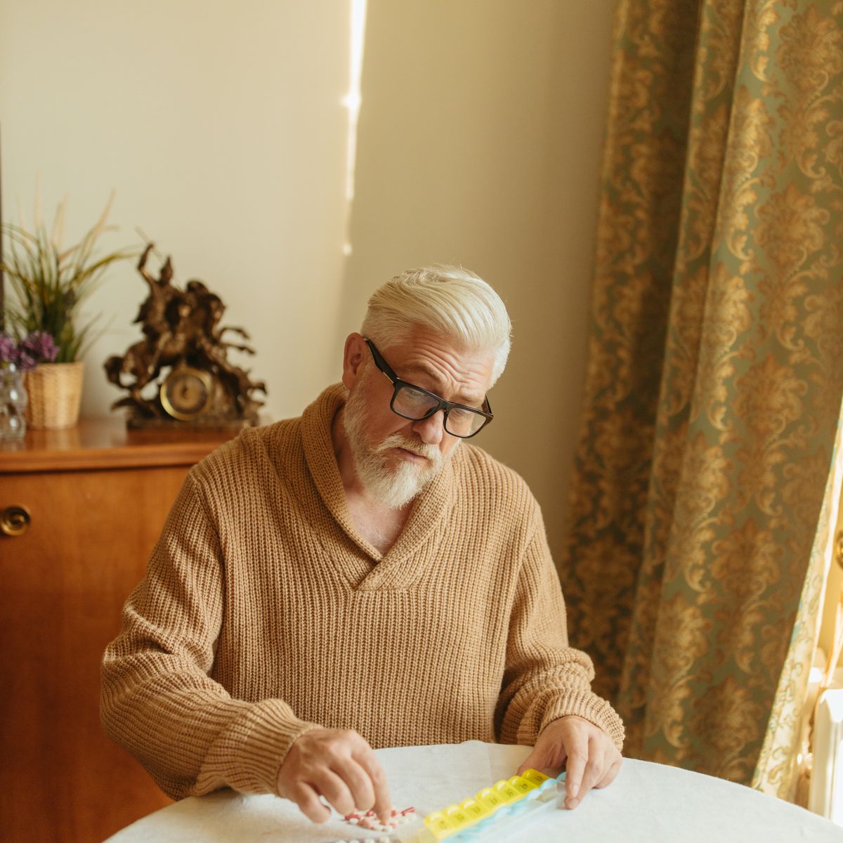 An older man organizing his daily medications into a pill organizer at home