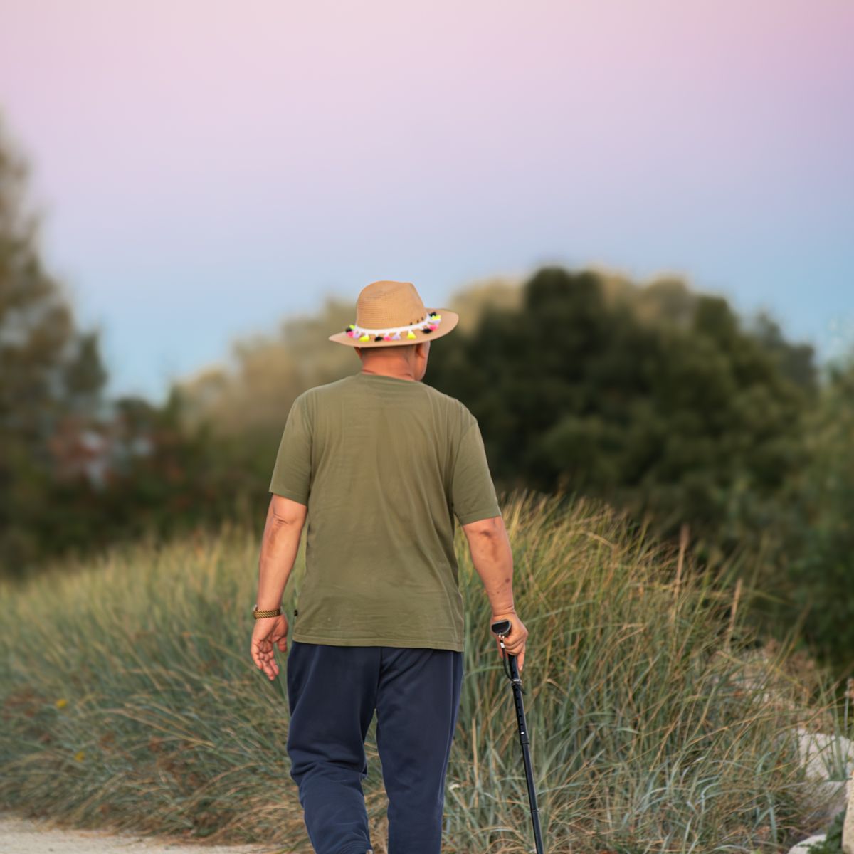 An older person walking outdoors with a cane for support